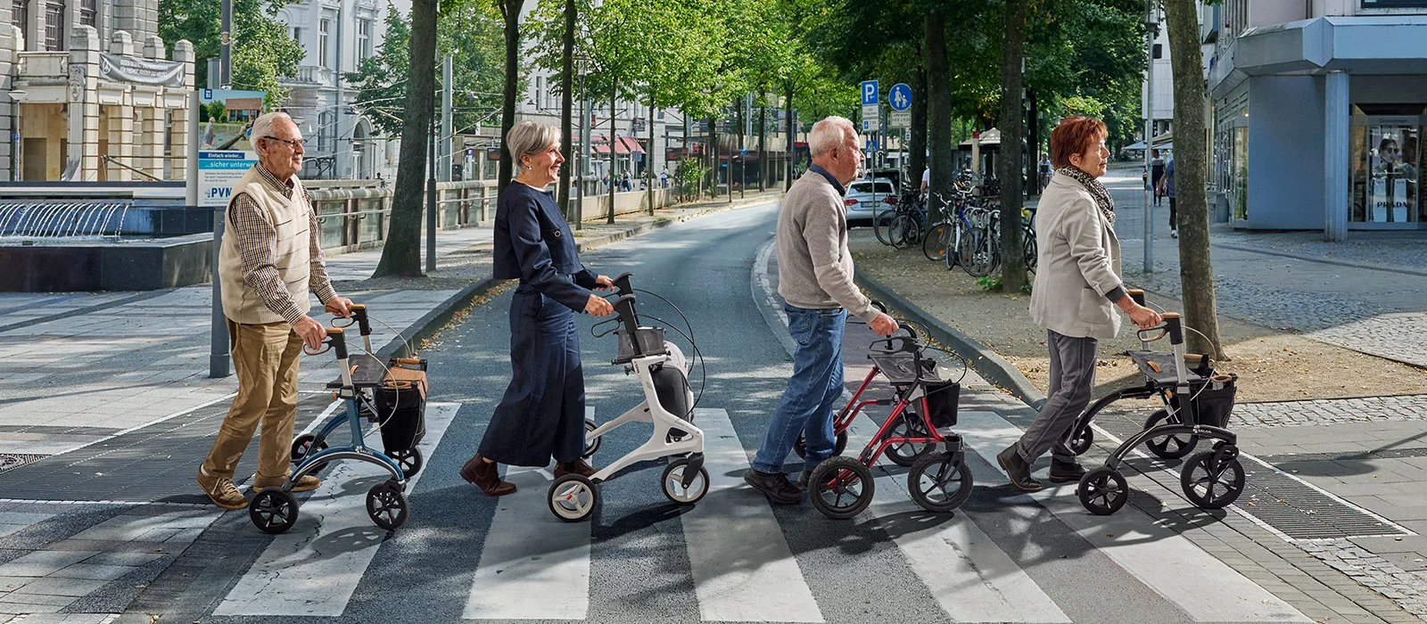 Vier Menschen mit Rollatoren überqueren hintereinander einen Zebrastreifen in der Bielefelder Innenstadt