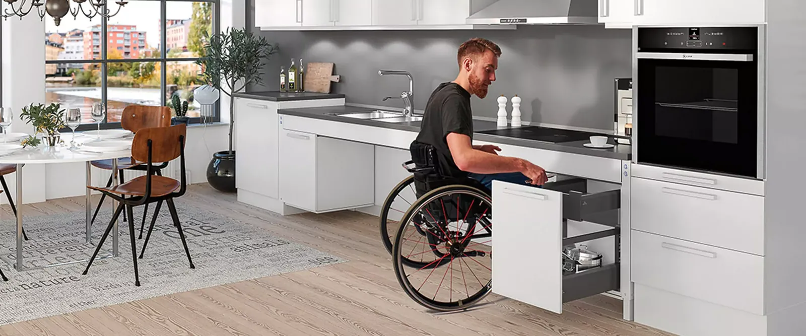 Barrierefreie Küche: ein Mann im Rollstuhl öffnet eine unterfahrbare Schublade