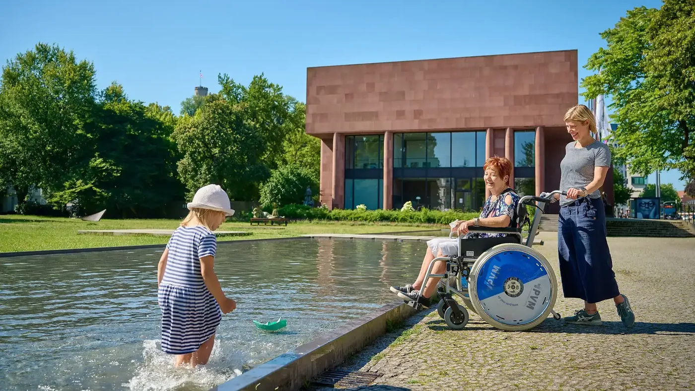Vor der Kunsthalle Bielefeld: eine Frau im Rollstuhl mit Begleiterin am Wasserbecken