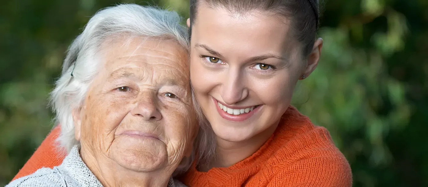 Eine junge Frau umarmt lächelnd eine ältere Frau
