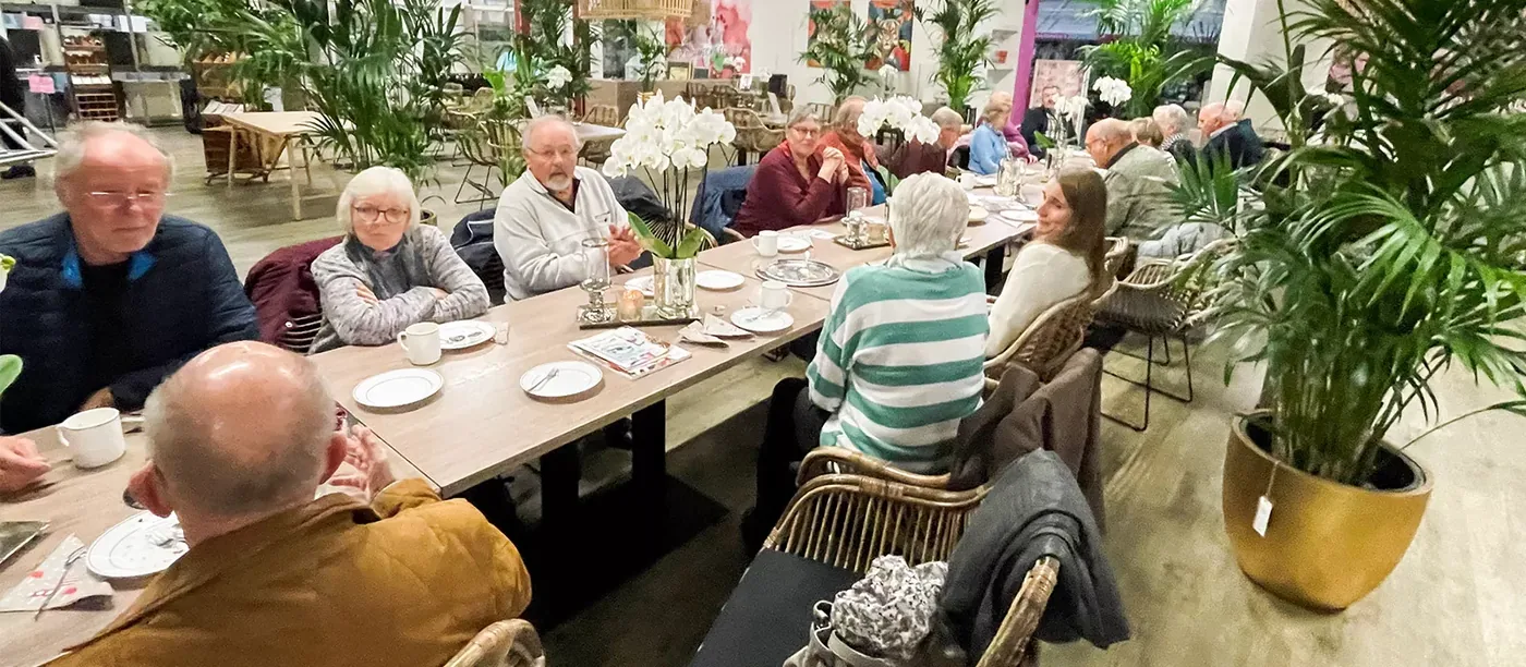 Eine Seniorengruppe sitzt an einer langen Tafel im Palmencafé
