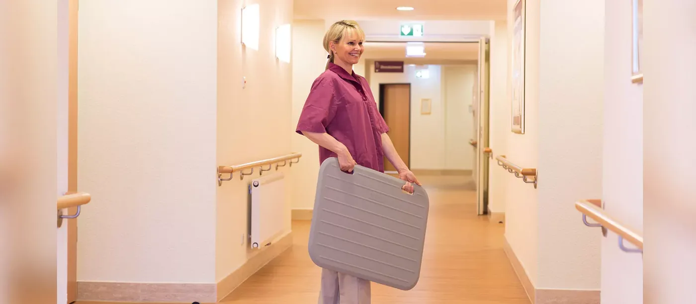 Eine Frau trägt eine Funk-Sensormatte durch einen Flur