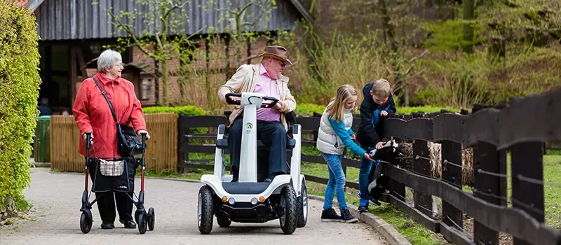Menschen mit Rollator und Elektromobil auf einem Spaziergang