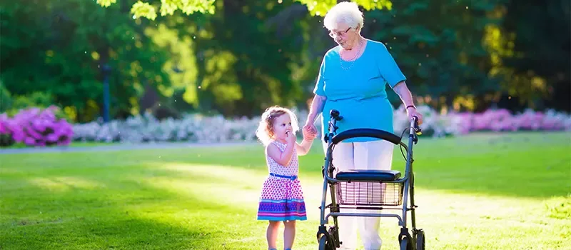 Eine Frau geht mit Rollator und Enkelin durch einen blühenden Park