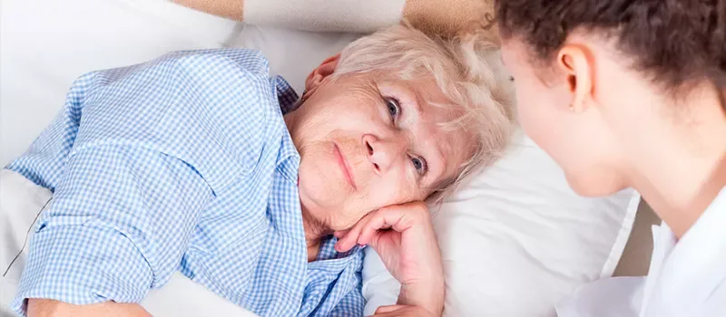 Eine Patientin im Pflegebett wird von einer Pflegerin betreut