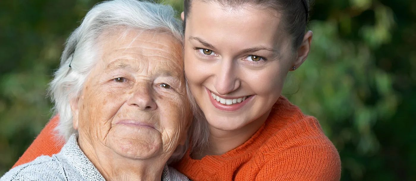 Eine junge Frau umarmt lächelnd eine ältere Frau