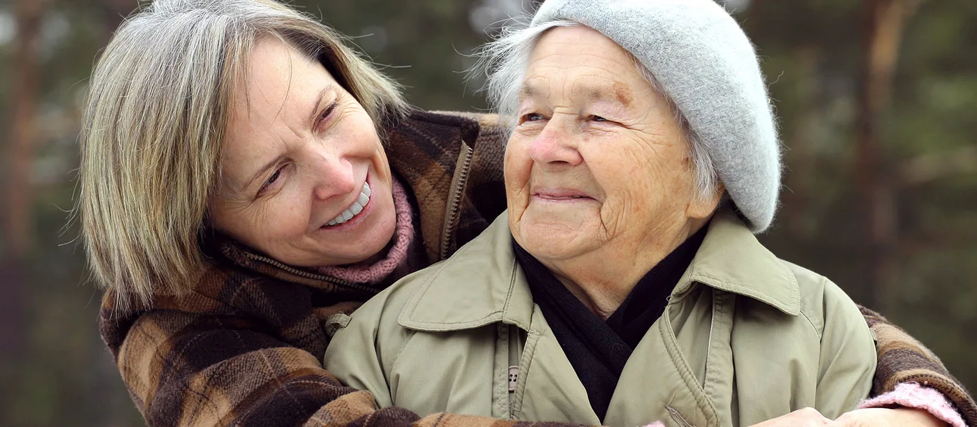 Eine Frau legt lachend den Arm um ihre ältere Mutter